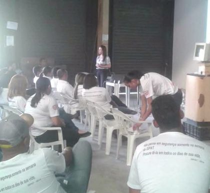 Funcionários de uniforme assistindo à palestra da SIPAT no galpão da empresa.